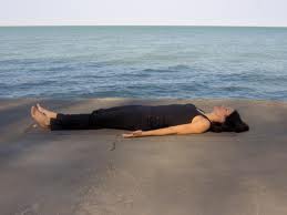 person lying in corpse pose near the water