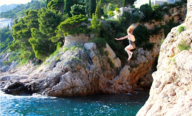woman jumping from a cliff into water